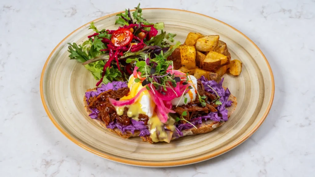 Poached eggs with hollandaise on sourdough toast with pulled braised filling, red cabbage, pickled onions and microgreens, served with roasted potatoes and salad
