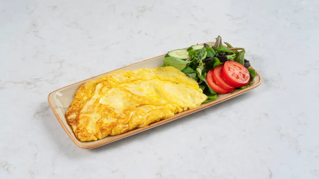 Golden vegetarian omelette served with mixed greens, cucumber and sliced tomatoes on a ceramic plate